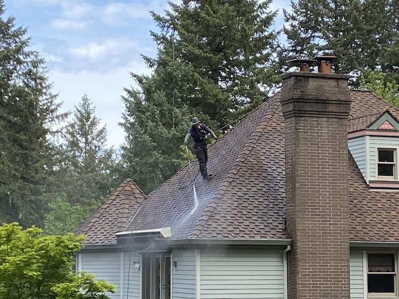 Roofer washing the debris off a roof in Portland, OR
